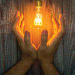 Hand with Glowing bulb on the wood background